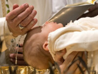 Ein Kind wird getauft. Auf dem Bild sieht man das Baby und die Hand des Taufspenders, der dem Kind das Wasser über die Stirn träufelt.