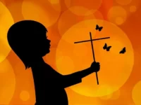 Eine moderne Zeichnung in Orangtöne gehalten. Auf der linken Seite des Bildes ein Schattenbild, das ein Kind darstellt. In der Hand ein Kreuz und um das Kreuz fliegen 3 Schmetterlinge.nee Im io.